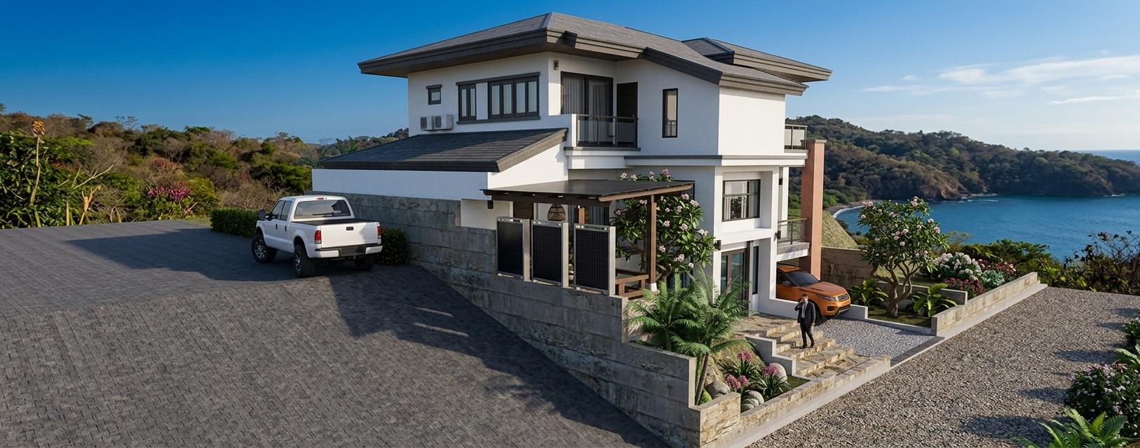 The photo captures a stunning two-story colonial classic residence bathed in the warm glow of a sunset, suggesting a peaceful spring evening. The exterior features crisp white walls with brown trim accents on the roofline and window frames, creating a timeless and elegant facade. A dark tiled roof with prominent overhangs adds to the classic architectural style. The property is situated on a gentle slope, with a well-maintained driveway leading up to the house. A white pickup truck is parked on the upper level of the driveway, while an orange sports car is visible in a covered carport on the lower level. Lush tropical landscaping, including palm trees and flowering bushes in vibrant pinks and purples, surrounds the entrance and terrace areas, enhancing the feeling of a serene, established home. Large windows, some with glass balconies, hint at well-appointed interior spaces, likely including a spacious living room, ready to welcome the fading light.