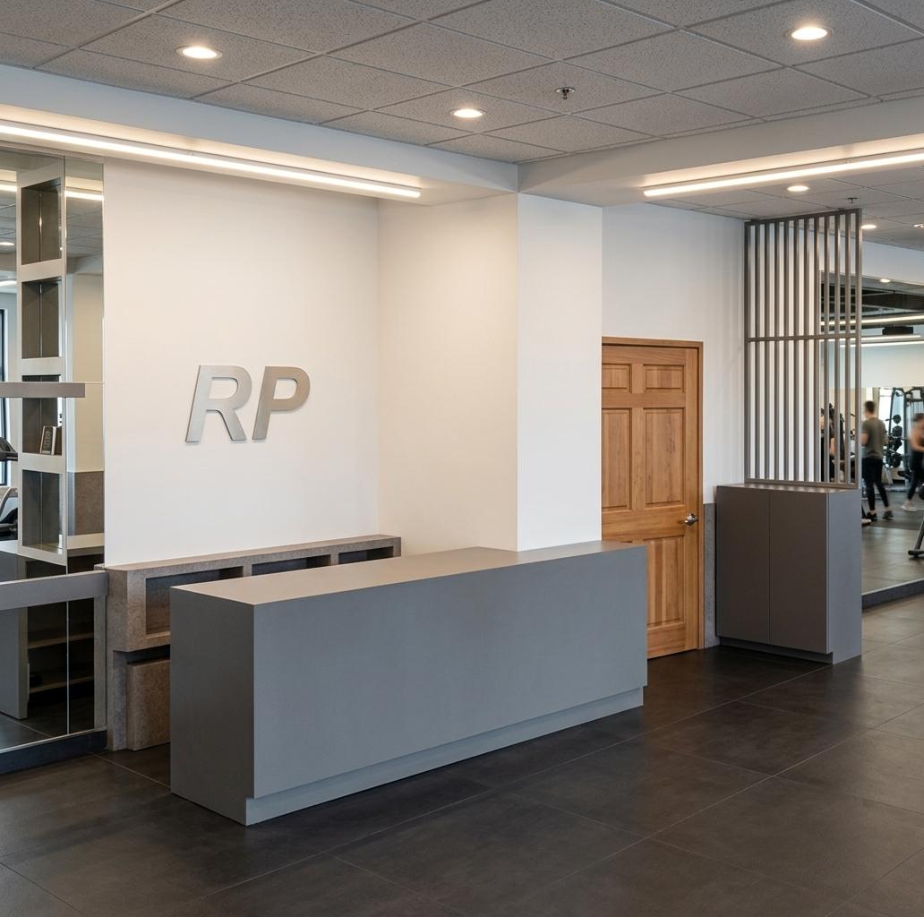 An incredibly lifelike, richly detailed, photorealistic eye-level interior perspective shot of a modern fusion fitness gym reception lobby set in an upscale urban athletic club. The scene is illuminated by crisp, warm-white linear LED strip lights recessed neatly along clean white structural beams, complemented by soft, focused halogen spotlight downlights embedded in the ceiling, creating a bright, energetic, and highly professional atmosphere. Captured with a 24mm wide-angle lens, emphasizing the clean lines, polished textures, and spatial depth of the reception area, the image showcases a minimalist, matte-gray monolithic reception desk sitting on a dark, seamless floor. On the pristine white wall behind the desk, the "RP" branding logo stands out with a subtle metallic sheen, flanked on the far left by a large, floor-to-ceiling mirror installation that reflects the gym's depth and doubles the visual space. To the right, a warm, paneled natural wood door adds an organic touch, contrasted by a newly introduced, sleek charcoal-gray shoe closet. Beside this closet, an elegant, open-slatted metal divider screen rises to the ceiling, effortlessly defining the entrance threshold of the gym without closing off the open-concept view or blocking the bright flow of light.