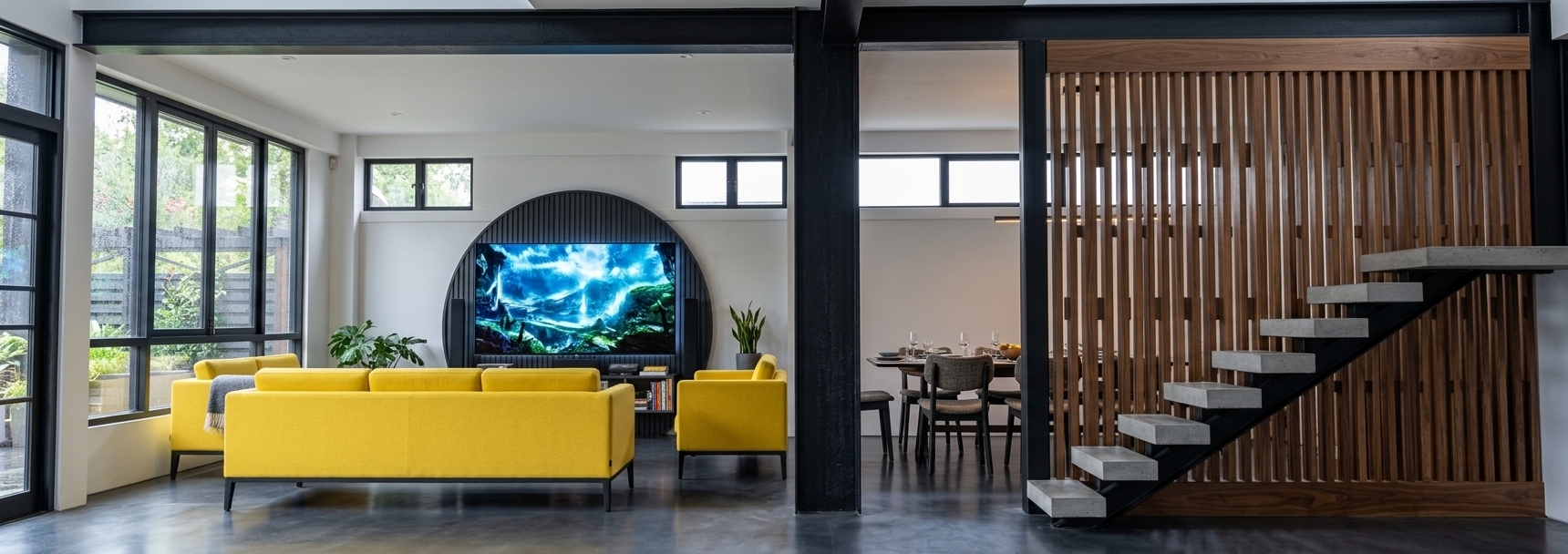 An incredibly lifelike, richly detailed, photorealistic wide-angle interior photo of a minimalist industrial living room with a techno wonderland aesthetic set in a modern open-plan loft conversion. The scene is illuminated by crisp, cool daylight filtering through high-level clerestory windows and expansive black-framed side glazing, balanced by a subtle, futuristic LED glow from the media center, creating a sophisticated and energetic atmosphere. Captured with a 24mm f/2.8 tilt-shift lens, emphasizing the rich tactile contrast between raw structural elements, warm timbers, and ultra-saturated fabrics. In the foreground, two sleek, linear sofas upholstered in brilliant canary-yellow wool crepe flank the seating area, resting on a seamless, charcoal-pigmented polished concrete floor that softly reflects the surroundings. The focal point of the lounge is a masterfully crafted circular media recess featuring deep-charcoal fluted wooden paneling, which frames a vibrant, ultra-high-definition television screen showcasing a luminous digital landscape. Massive matte-black steel structural columns and overhead beams anchor the space, seamlessly separating the main living area from a minimalist dining nook in the background. To the right, a floating architectural staircase constructed from raw gray concrete treads and sleek black steel rises elegantly against an expansive partition wall of vertical walnut slats, adding a warm, rhythmic organic texture that beautifully contrasts with the cold, high-tech industrial aesthetic of the home.