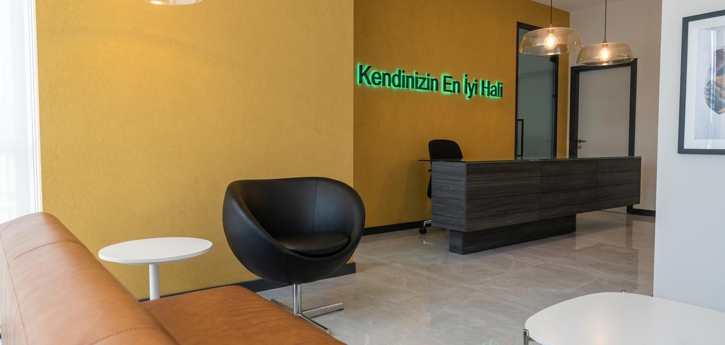 An incredibly lifelike, richly detailed, photorealistic wide-angle interior shot of a modern white doctor clinic reception and waiting lounge set in an upscale minimalist haven. The scene is illuminated by soft, ambient daylight blended with warm translucent pendant glows and vibrant neon backlighting, creating a calm, luxurious hotel-lobby atmosphere. Captured with a 35mm prime architectural lens, emphasizing subtle wall textures, refined leather surfaces, and crisp geometric lines, the composition highlights a striking textured mustard-yellow accent wall adorned with glowing emerald-green backlit typography reading "Kendinizin En İyi Hali." Beneath it sits a sophisticated floating reception desk clad in dark charcoal wood grain with polished glass surfaces. In the foreground, a comfortable cognac tan leather bench and a sleek matte-black swivel tub armchair surround a minimalist white pedestal side table, all set upon polished, large-format light gray porcelain floor tiles that catch soft, realistic reflections from the ambient lights above.
