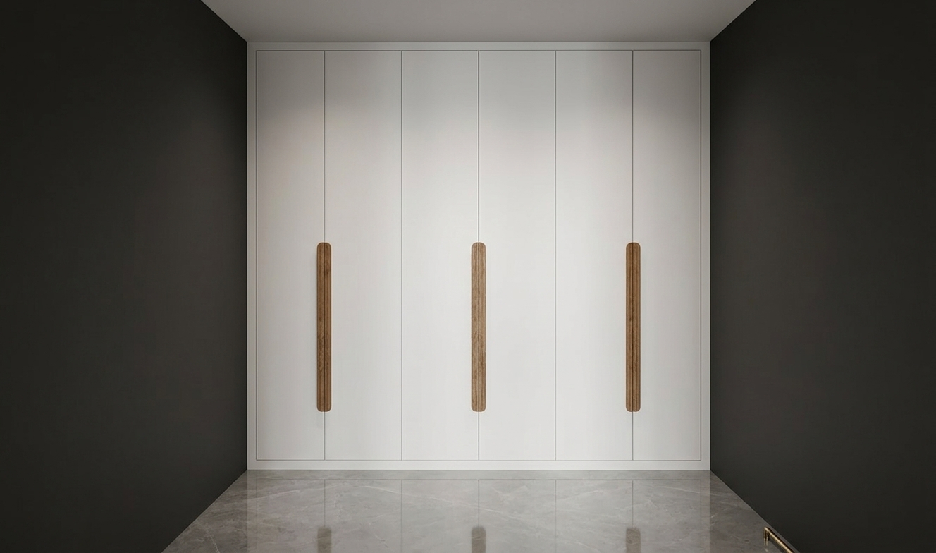 An incredibly lifelike, richly detailed, photorealistic eye-level interior shot of a bespoke wardrobe in a minimalist walk-in closet set in a contemporary luxury residence. The scene is illuminated by soft, recessed architectural ceiling lighting that casts gentle vertical gradients down the cabinetry, creating a tranquil and refined atmosphere. Captured with a 35mm architectural lens, emphasizing the satin-matte white panel surfaces, finely grained natural warm oak handles, and the subtle reflections on the polished grey marble floor. The seamless floor-to-ceiling wardrobe doors are flanked by matte charcoal-toned walls, creating a balanced, high-contrast framing that highlights the clean lines and understated elegance of this modern storage haven.