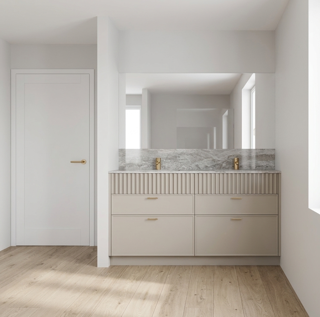 A photorealistic architectural interior photograph of the bathroom vanity scene captured in bright, natural midday daylight. The rendering showcases tactile textures: realistic grain on the light oak plank flooring, a smooth matte finish on the warm greige cabinetry with soft shadows in the fluted detailing, authentic veining and polished sheen on the stone countertop, and subtle metallic luster on the brushed brass faucets and slim pulls. Diffuse, neutral midday light illuminates the clean walls and white door evenly, creating soft contact shadows, gentle mirror reflections, and a crisp, lifelike photographic depth of field.