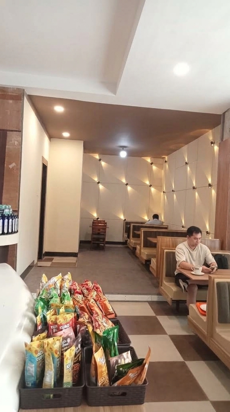 Update the cafe interior: change the back panelled accent walls featuring the sconce lights to a smooth, elegant cream color while retaining the warm lighting effect. Repair and finish the damaged, exposed white ceiling in the foreground so it becomes a uniform, clean, flat white painted ceiling. Keep all other elements, including the brown upper back ceiling, wooden booths, snack baskets, and customers, unchanged.