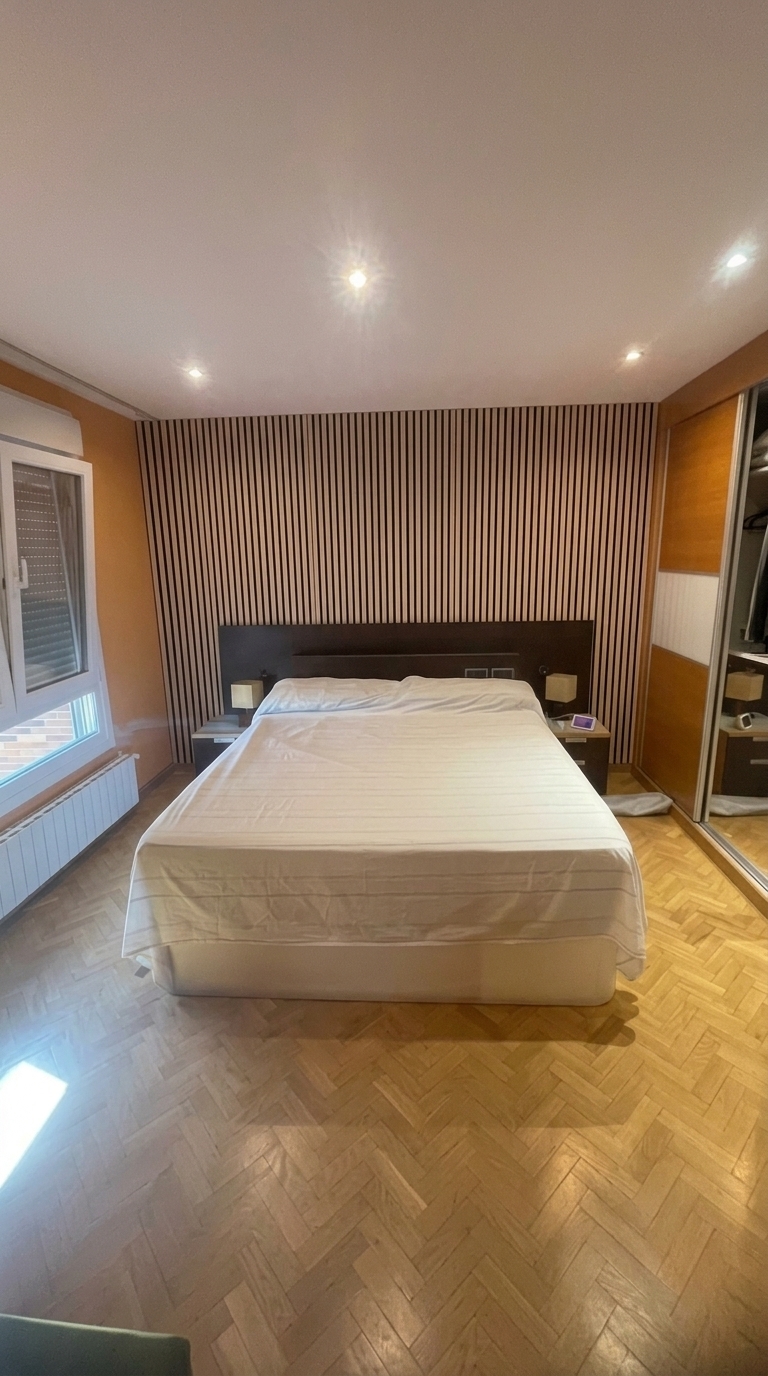A photorealistic 3D architectural render of this bedroom with improved, centered, eye-level wide-angle framing. Maintain the exact layout, colors, and furniture: the bed with white bedding (remove loose items like the laptop and tape measure), the dark wooden headboard with matching nightstands and small lamps, herringbone wood parquet flooring, white ceiling with recessed spotlights, the window on the left, and the sliding mirror-door closet on the right. Cover the entire orange accent wall behind the bed from floor to ceiling with a modern decorative wood slat wall paneling.