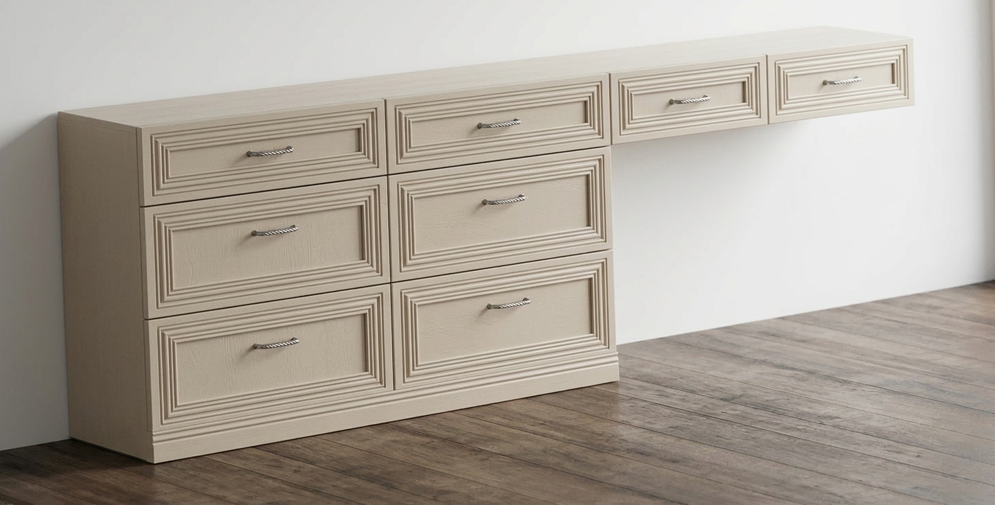 Architectural photograph of the cream-toned fitted desk and drawer unit, precisely maintaining the geometry, camera angle, and composition. Bright, clean midday daylight fills the space from an off-camera window, casting defined yet soft contact shadows beneath the floating extension and across the matte dark wood floor. The cabinetry exhibits a smooth satin-painted finish with subtle surface micro-textures, revealing sharp ambient occlusion within the recessed drawer mouldings, while the brushed metal handles catch gentle specular highlights. Photographed with a crisp 50mm architectural lens, displaying neutral color temperature, balanced exposure, and natural material textures throughout.