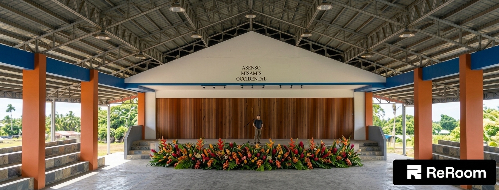 A photorealistic architectural capture of the open-air pavilion under bright, harsh midday summer sunlight. Intense overhead natural daylight floods the perimeter, casting sharp, deep shadows beneath the steel roof trusses and eaves while naturally illuminating the concrete floor and vibrant floral arrangement. The painted orange columns, wooden slatted backdrop, and textured stone steps display authentic material physics, including faint surface scuffs, micro-texture in the wood grain, and realistic dust along the edges. Captured with an eye-level wide-angle lens, showing crisp focal depth, subtle atmospheric haze in the sunlit background, realistic exposure balance between the shaded interior and bright exterior, and delicate photographic grain.