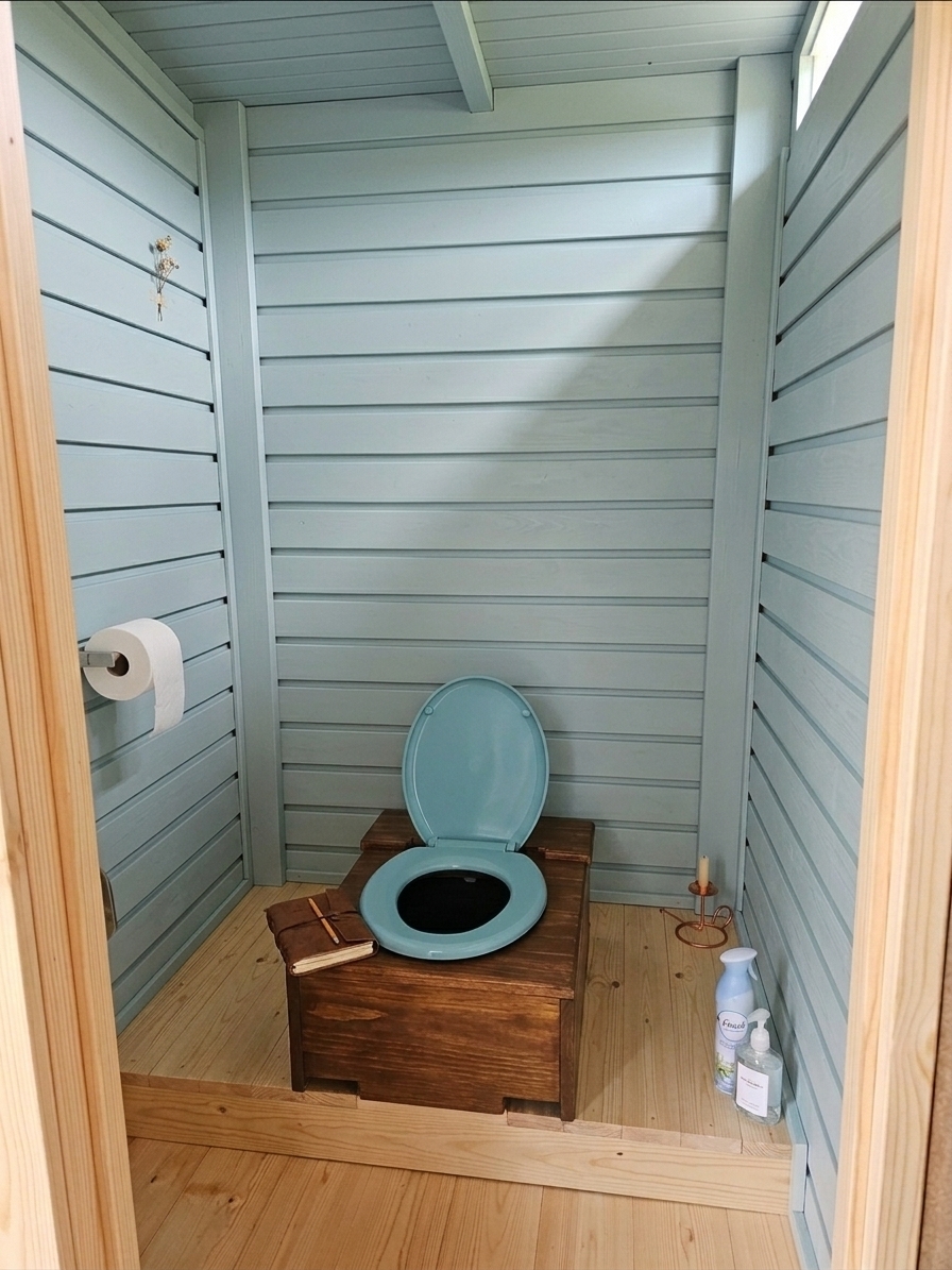 A crisp interior photograph maintaining the exact composition, perspective, and layout of the cabin, updating the horizontal wall paneling to cleanly spaced wooden slats finished in a soft, muted pastel paint that subtly reveals the natural wood grain underneath. Soft, diffused daylight filters from above, casting gentle shadows within the recessed gaps between the slats and illuminating the wooden base, seat, and floor with balanced, natural contrast. Captured with a standard 35mm lens, the scene features authentic micro-textures, delicate dust particles in the ambient light, and lifelike photographic depth without altering the geometry or placement of existing objects.