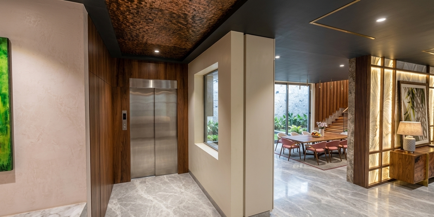A wide-angle architectural photograph capturing the modern interior hallway exactly as arranged, centered on the elevator entrance. Soft, warm recessed ceiling lights and gentle cove illumination wash down over the textured ceiling and the rich, natural grain of the wood paneling surrounding the brushed stainless steel elevator doors. The polished grey marble floor reflects subtle ambient light from the ceiling fixtures. Crisp matte white walls frame the view into the adjacent dining space and decorative partition screen, balanced by soft natural daylight from the background windows. Captured on a sharp architectural lens with realistic depth of field, delicate specular highlights, and natural shadow transitions for an authentic high-end interior feel.