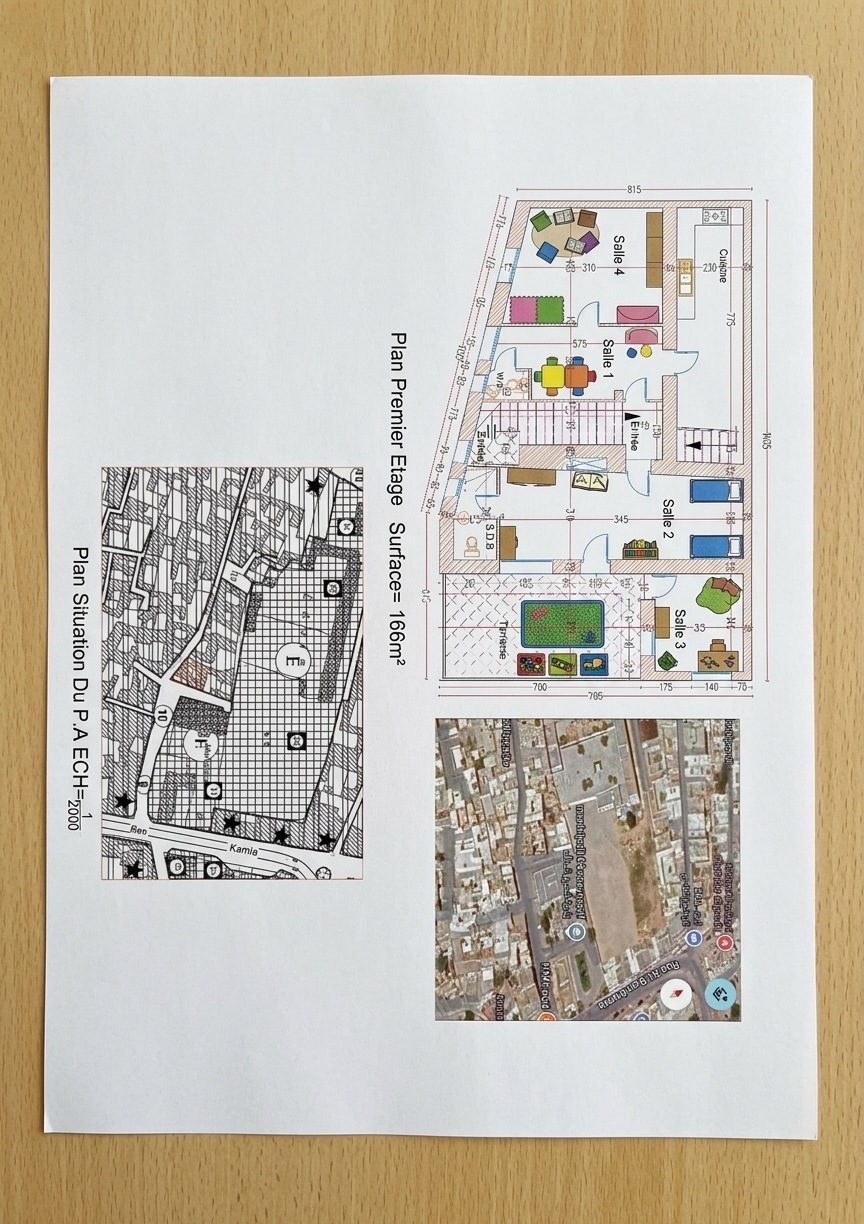 A sharp, overhead flat-lay photograph of the architectural sheet printed on matte paper under soft, diffused daylight. Retain the exact technical drafting layout, dimensions, cadastral map, and aerial image, updating the room annotations to read Salle 1, Salle 2, Salle 3, and Salle 4 in matching clean black technical lettering for a daycare space. Captured with a 50mm lens at f/8 with crisp focus across the page, showing tactile paper grain, subtle ink absorption, and natural print texture.