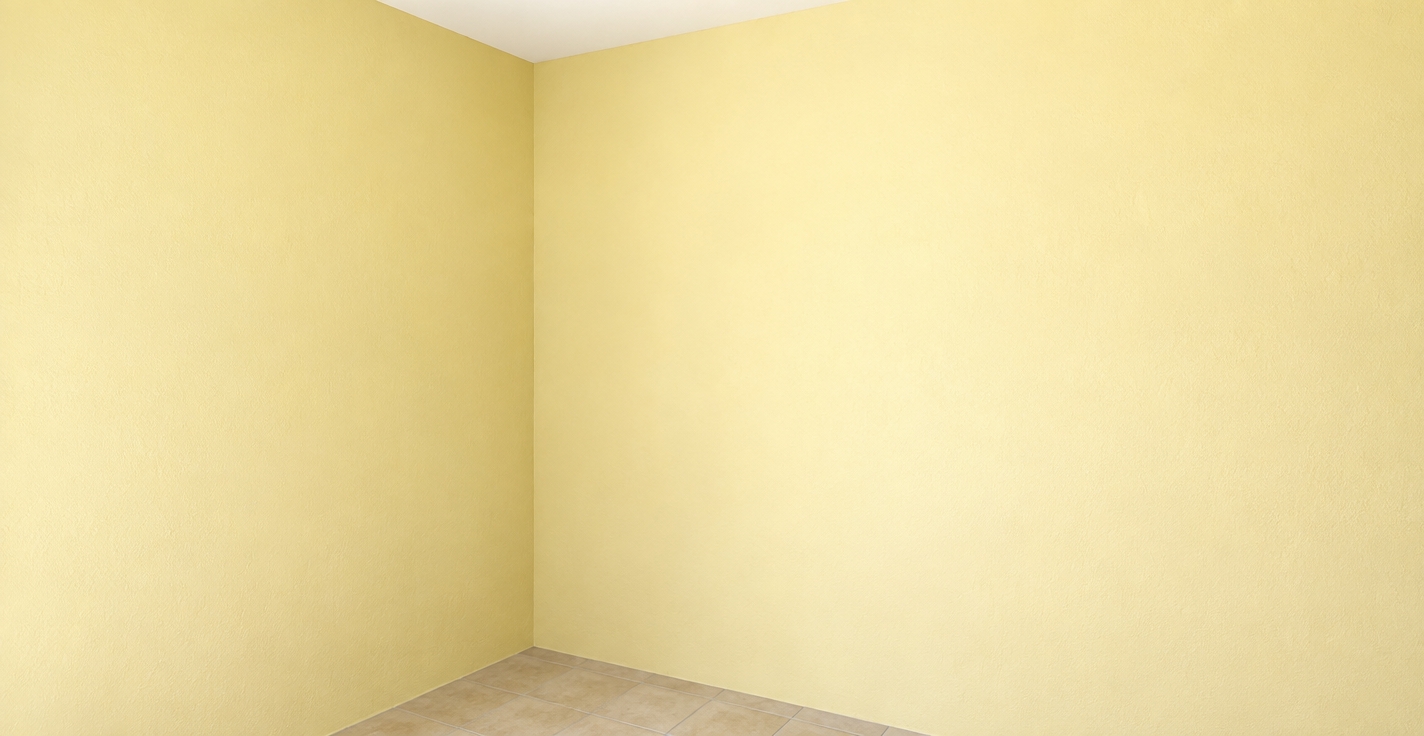 A crisp, eye-level photograph of the empty interior corner, faithfully preserving the exact geometry, pale yellow walls, white ceiling, and tiled floor. Natural daylight casts soft ambient illumination across the matte-painted drywall, revealing subtle roller stipple textures and minor surface variations. The beige ceramic floor tiles show realistic grout lines, delicate stone grain, and faint specular sheen under a 35mm architectural lens, complemented by natural ambient occlusion in the wall creases, gentle corner vignetting, and fine photographic grain.