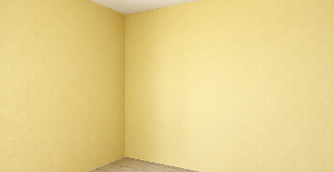 Capture this empty room corner as a crisp architectural photograph, strictly maintaining the exact geometry, perspective, and materials. The pale yellow walls feature realistic matte paint texture with subtle drywall micro-imperfections and gentle light falloff, meeting at a softly shadowed corner seam. Below, the beige floor tiles exhibit authentic ceramic sheen, realistic grout lines, and faint ambient reflections. The white ceiling transition remains sharp and clean under soft, warm interior daylight, finished with natural tonal depth and subtle photographic grain.