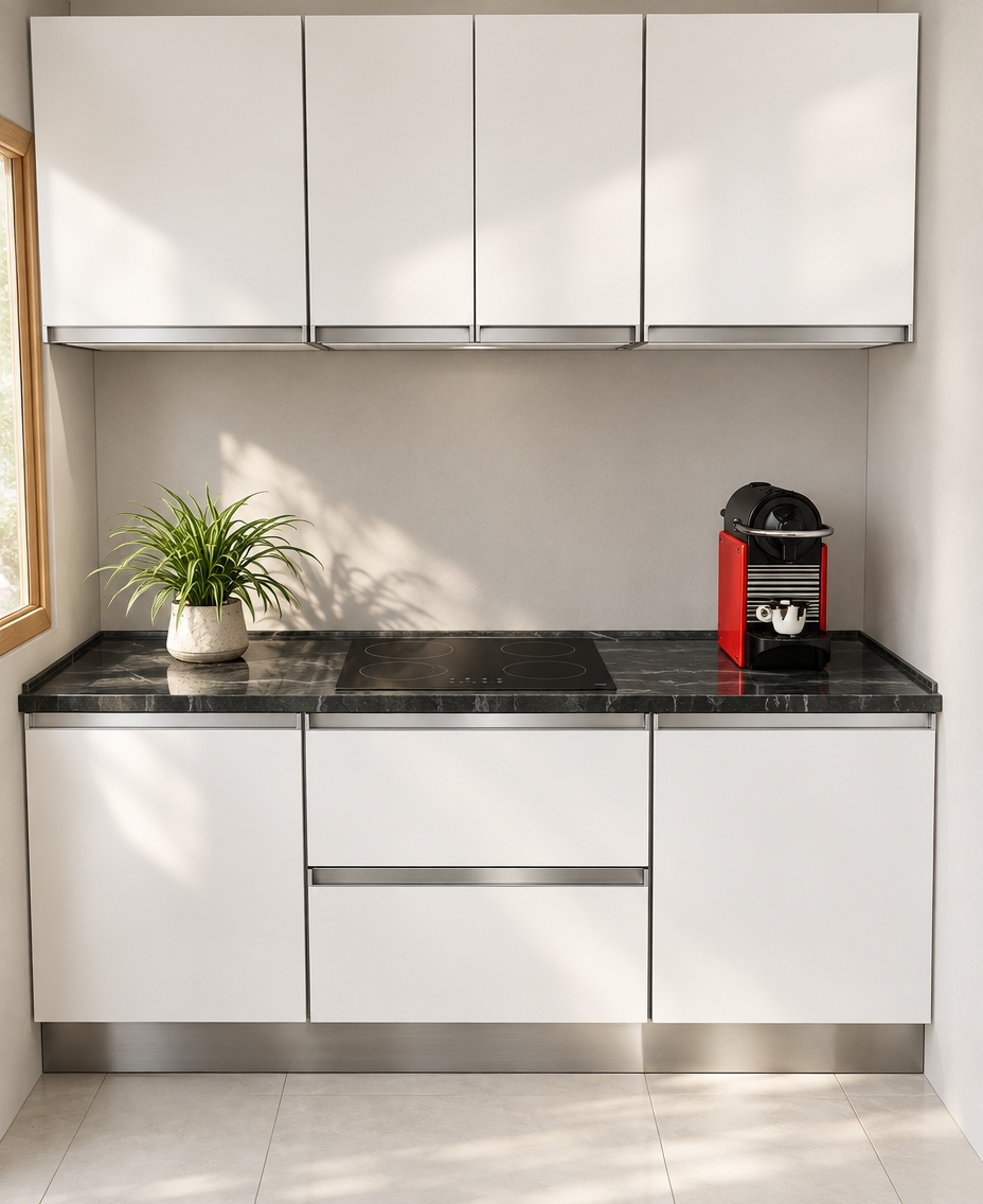 An incredibly lifelike, richly detailed, photorealistic eye-level interior shot of a minimalist kitchenette set in a serene Scandinavian sanctuary. The scene is illuminated by soft, diffused morning light streaming from a nearby window, creating a crisp, airy, and tranquil atmosphere. Captured with a 35mm lens, emphasizing the tactile contrast between the matte-finish, arctic-white cabinetry and the dramatic, deep-charcoal marble countertop with its subtle, flowing white veining.

The kitchen features sleek, handleless cabinetry with polished chrome recessed profiles that catch the light, adding a touch of understated sophistication. A vibrant red espresso machine adds a singular, sharp pop of color against the monochromatic palette, perfectly balanced by a lush, potted spider plant in a textured ceramic vessel. The integrated black induction cooktop sits seamlessly flush with the stone surface, reflecting the soft ambient light. Below, a brushed stainless-steel kickplate grounds the units against clean, oversized pale porcelain floor tiles, evoking a sense of refined, uncluttered Nordic living where functionality meets quiet, modern elegance.