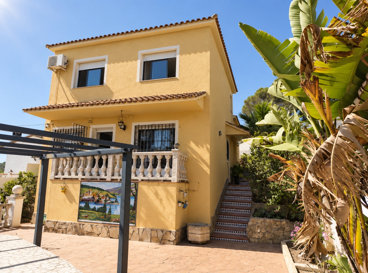 A photorealistic architectural photograph capturing the exact scene and composition of the two-story house under bright, direct Mediterranean midday sunlight with a clear blue sky. The exterior stucco walls are repainted in a matte RAL 1002 sand yellow with fine mineral texture, while the natural stone foundation, staircase masonry, tiled steps, and ceramic wall mural remain untouched in their authentic weathered state. Window frames and doors feature a clean semi-gloss white finish, contrasting with the metal pergola, window security bars, railings, and fixtures, which are finished in smooth matte black. Crisp diagonal shadows fall across the facade from the roofline and adjacent lush banana palms, captured with sharp optical clarity, subtle lens flare, natural film grain, and fine surface textures throughout.